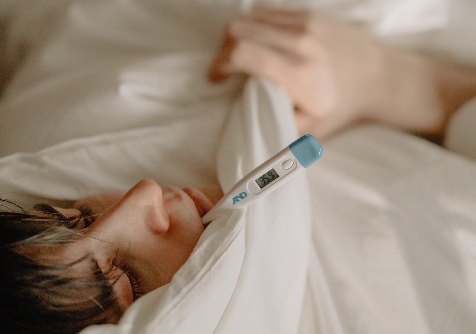 Sick person lying in bed with a thermometer