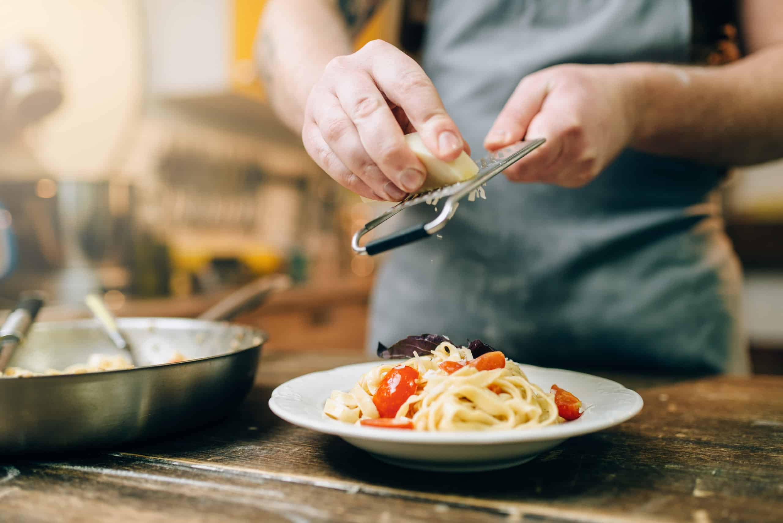 Chef grates cheese to the plate with fresh pasta